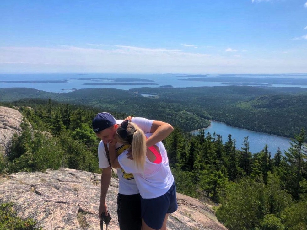 Patricia and Nikolas hugging on a summit above a lake and islands